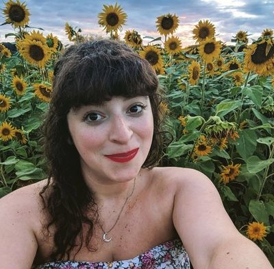 A woman smiling in a sunflower field at sunset.
