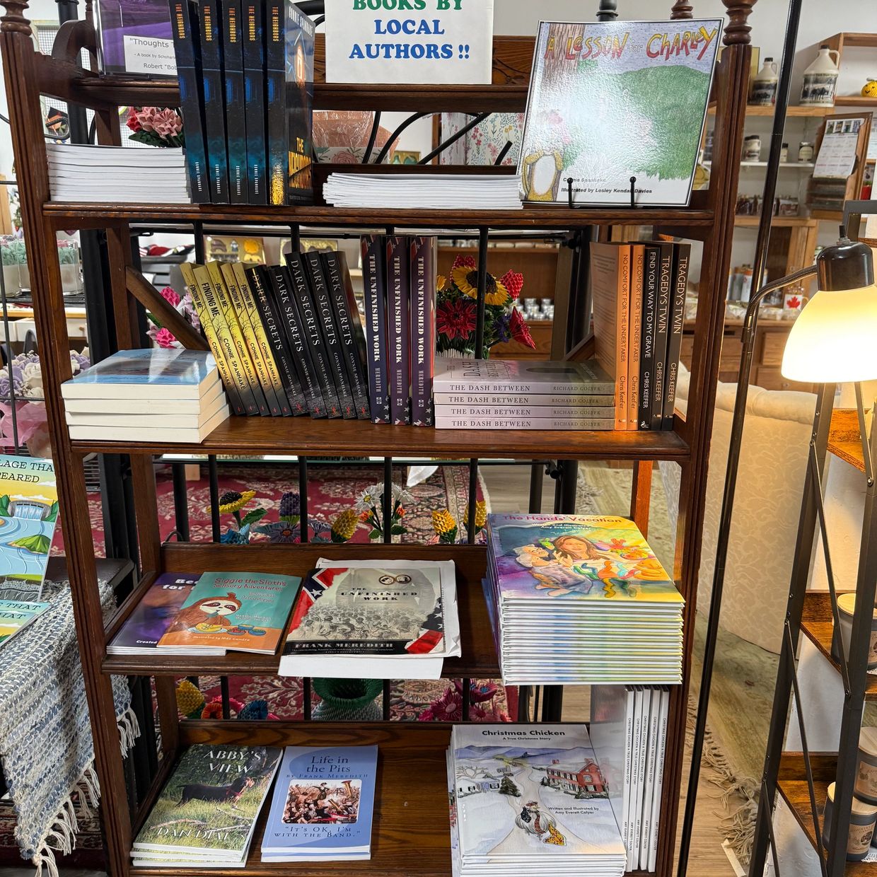 A wooden shelf displaying books by local authors in a cozy bookstore.