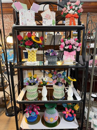 Colorful handcrafted flower arrangements on a black metal shelf.