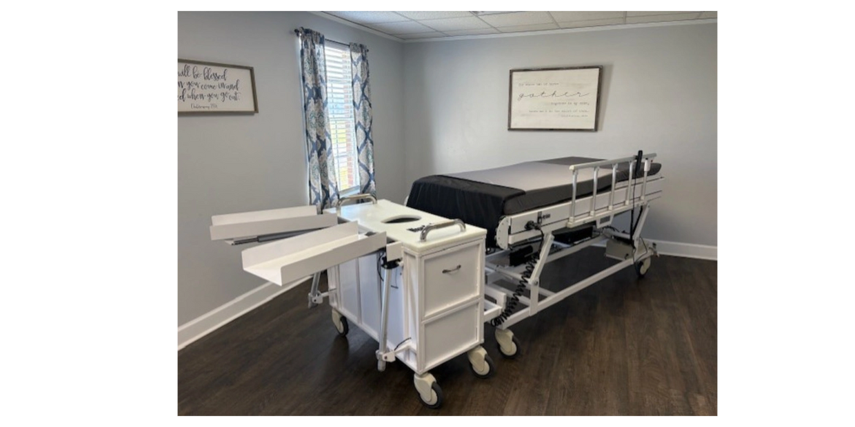 A medical examination table with adjustable sections and attached trays on wheels.