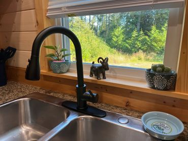 Kitchen sink with small plants and view of forest through the window. Friendly goat included!
