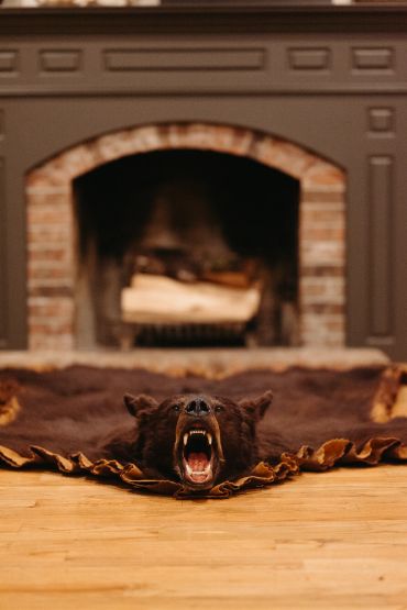 A roaring bear rug in front of a fireplace.