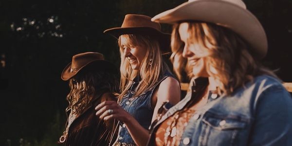 Three women wearing cowboy hats outdoors.