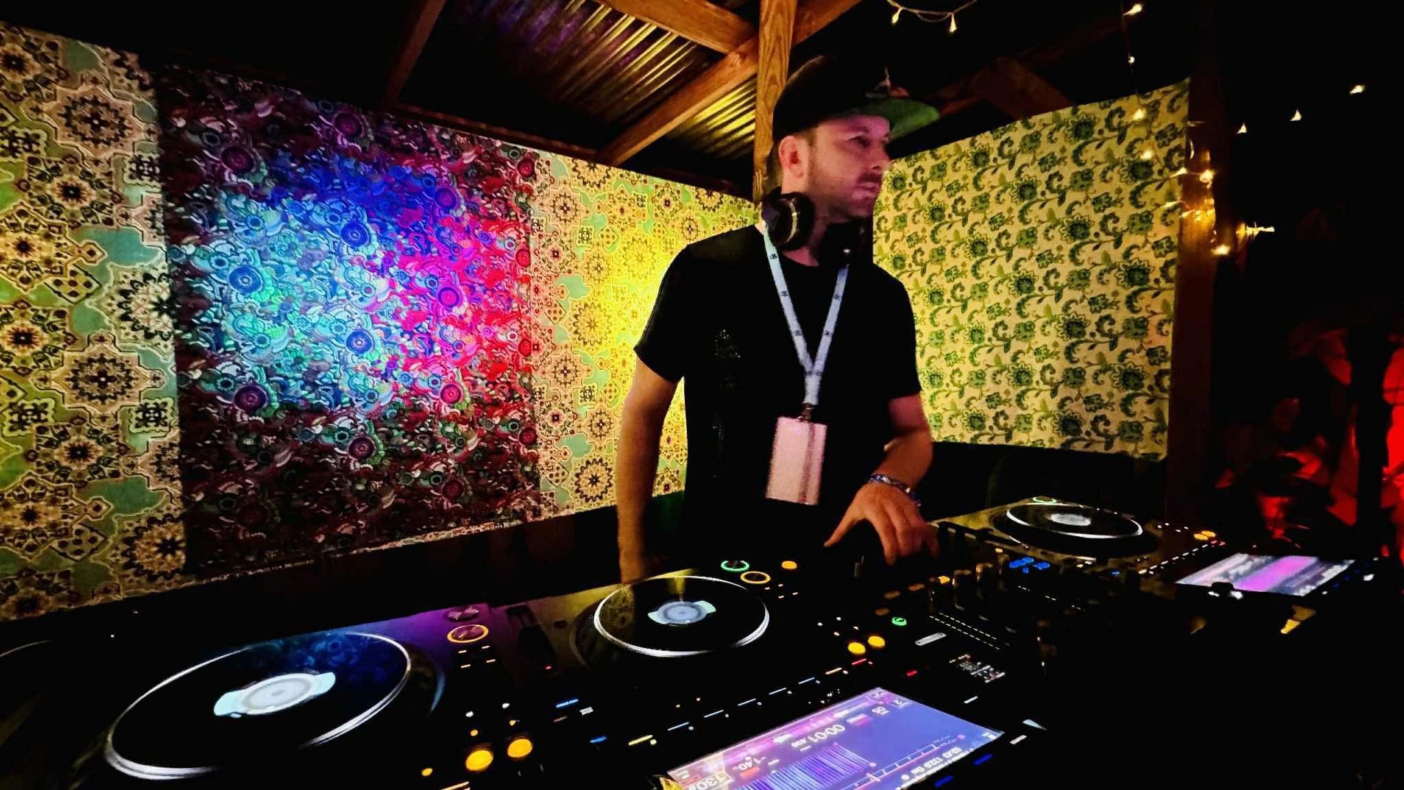 A DJ performing in a colorful, patterned booth with vibrant lighting.