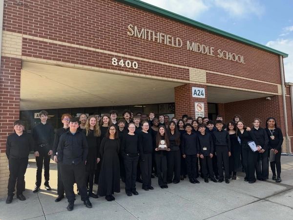 Middle school group dressed in black posing with a trophy outside their school.