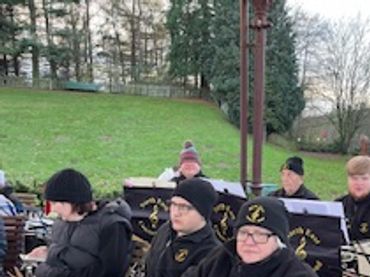 A group of musicians in black winter clothing sitting outdoors with instruments.