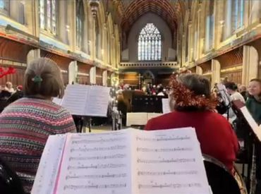 Musicians rehearsing inside a grand church with high ceilings and stained glass windows.