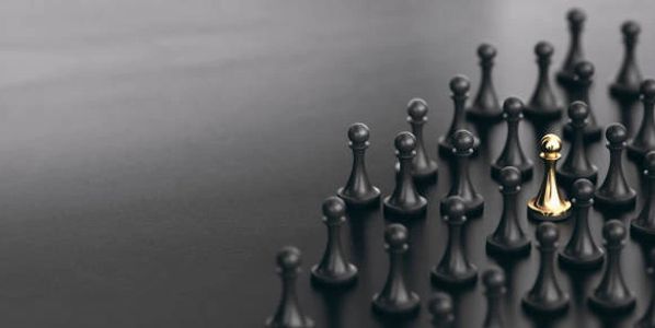 A golden chess pawn stands out among many black pawns on a dark surface.