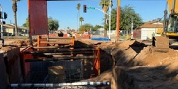 Construction site with deep trench and heavy machinery under clear sky.