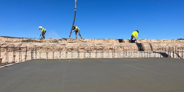 Three construction workers smoothing freshly poured concrete under a clear blue sky.