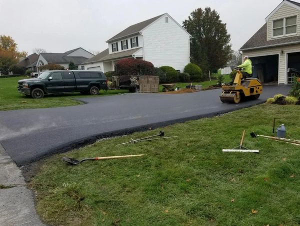 Worker smooths fresh asphalt driveway in a residential neighborhood.