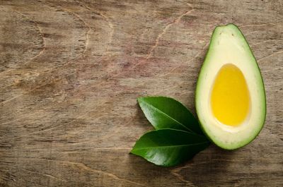 Half an avocado with a yellow pit and green leaves on a wooden surface.