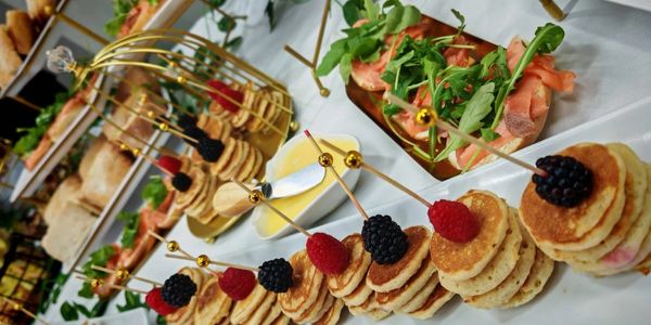 Mini pancakes con frutos rojos y canapés variados en una mesa.