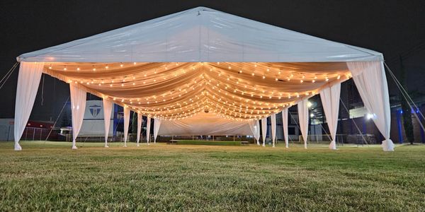 Carpa blanca con luces colgantes en un campo.