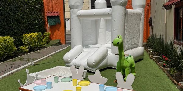 Mesa de fiesta infantil con castillo inflable blanco y dinosaurio verde.