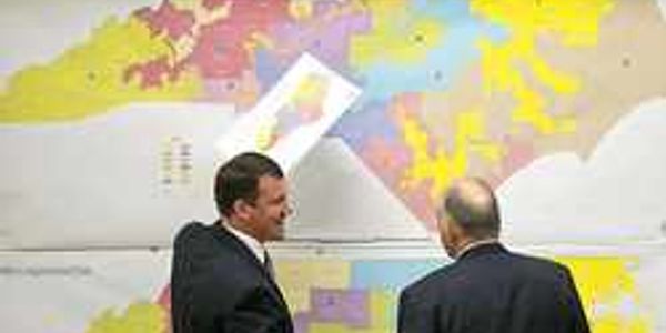 Two men in suits examining a large colorful map on the wall.