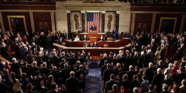 A formal gathering in the US Capitol with attendees raising their hands.
