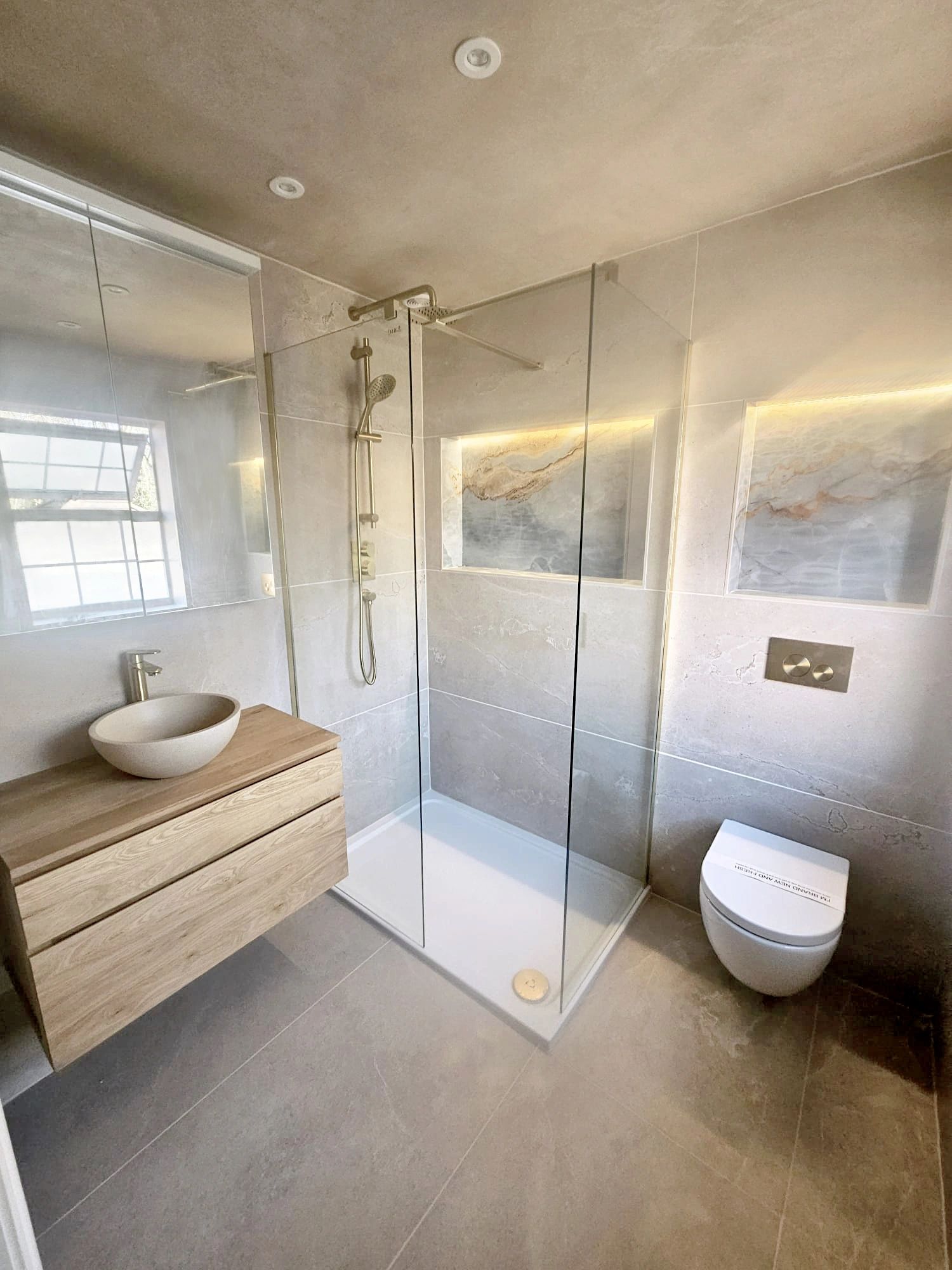 Modern bathroom with glass shower, wooden vanity, and wall-mounted toilet.