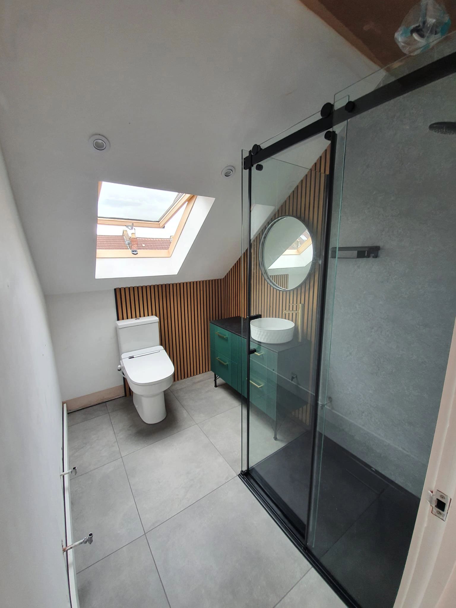 Modern bathroom with skylight, glass shower, and wooden accent wall.