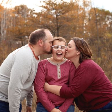 Parents kissing their laughing son outdoors in autumn.
