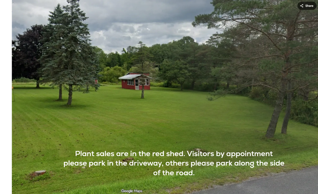 A red shed on a green lawn with a sign about plant sales and parking instructions.