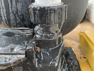 A wet black mechanical component with a white fitting on top.