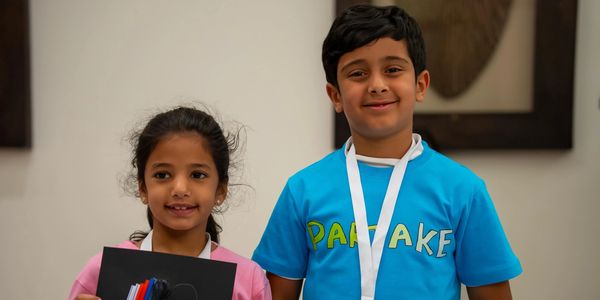 Two children smiling, wearing medals, and holding an award certificate.