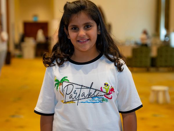 A smiling girl wearing a white Partyaki t-shirt with colorful designs.