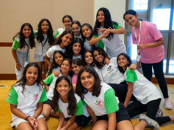 A cheerful group of young girls posing indoors, many wearing matching green and white shirts.