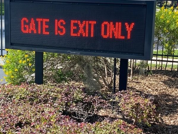 Electronic LED sign displays "GATE IS EXIT ONLY" at a gated community entrance./ Pending approval