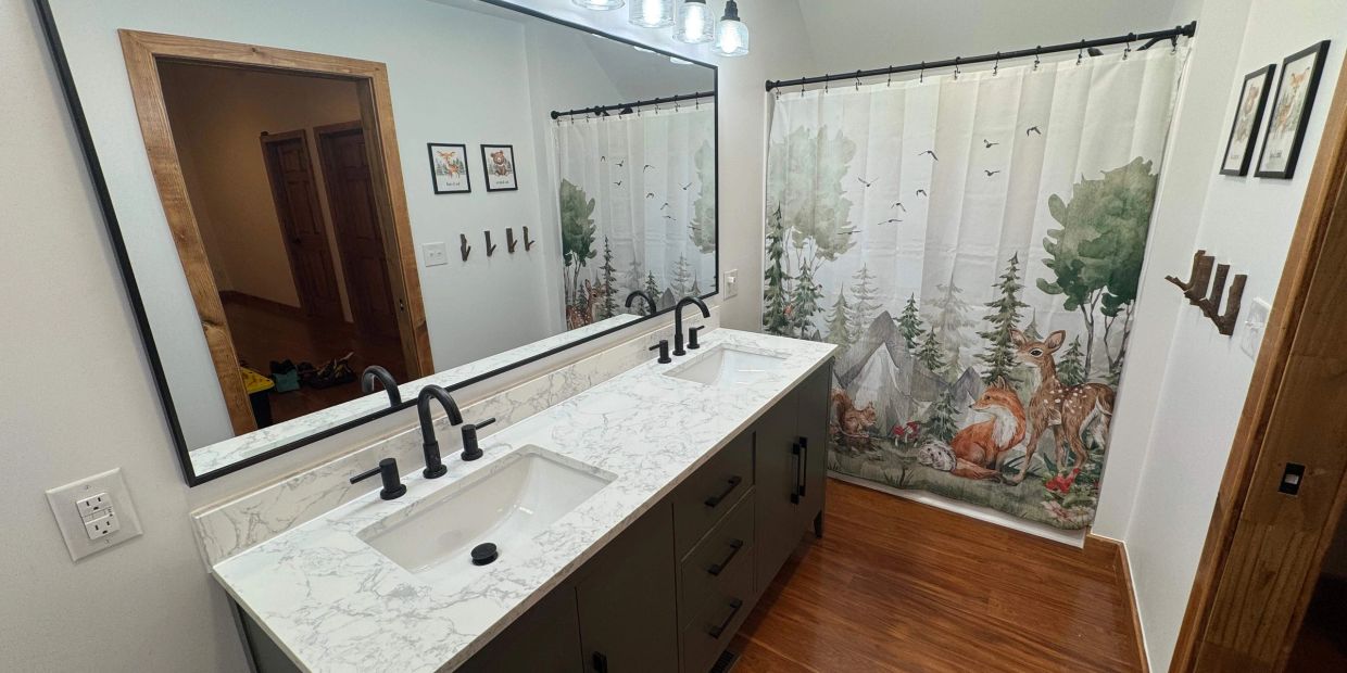 Modern bathroom with double sink and forest-themed shower curtain.