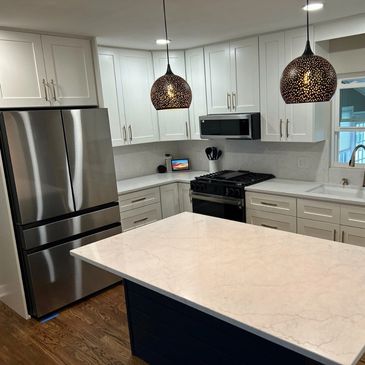 Clean marble countertop kitchen with dark island and stainless steel appliances 