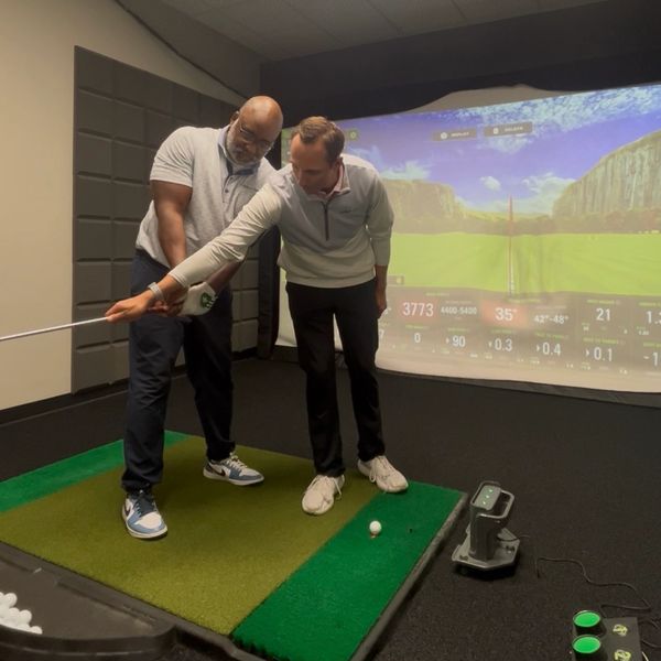 Two men practicing golf indoors with a simulator.