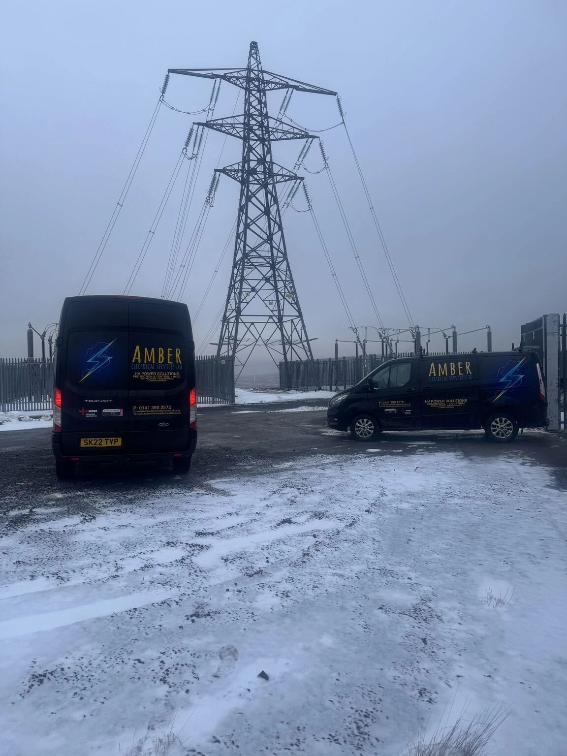 Two Amber Electrical Services vans parked near an electrical pylon in snowy weather.