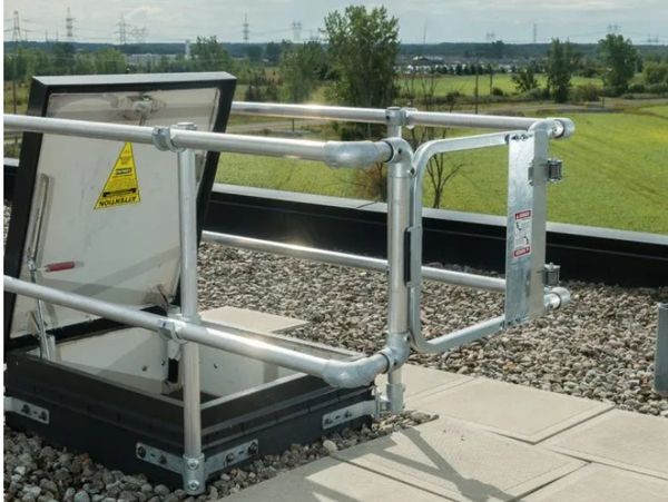 Safety railing around an open rooftop hatch with warning signs.