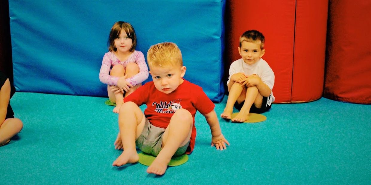 Three children sitting on colored spots in a playroom.