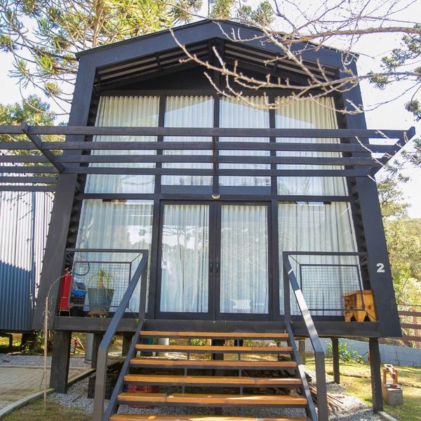 Modern black cabin with large glass windows and wooden stairs.