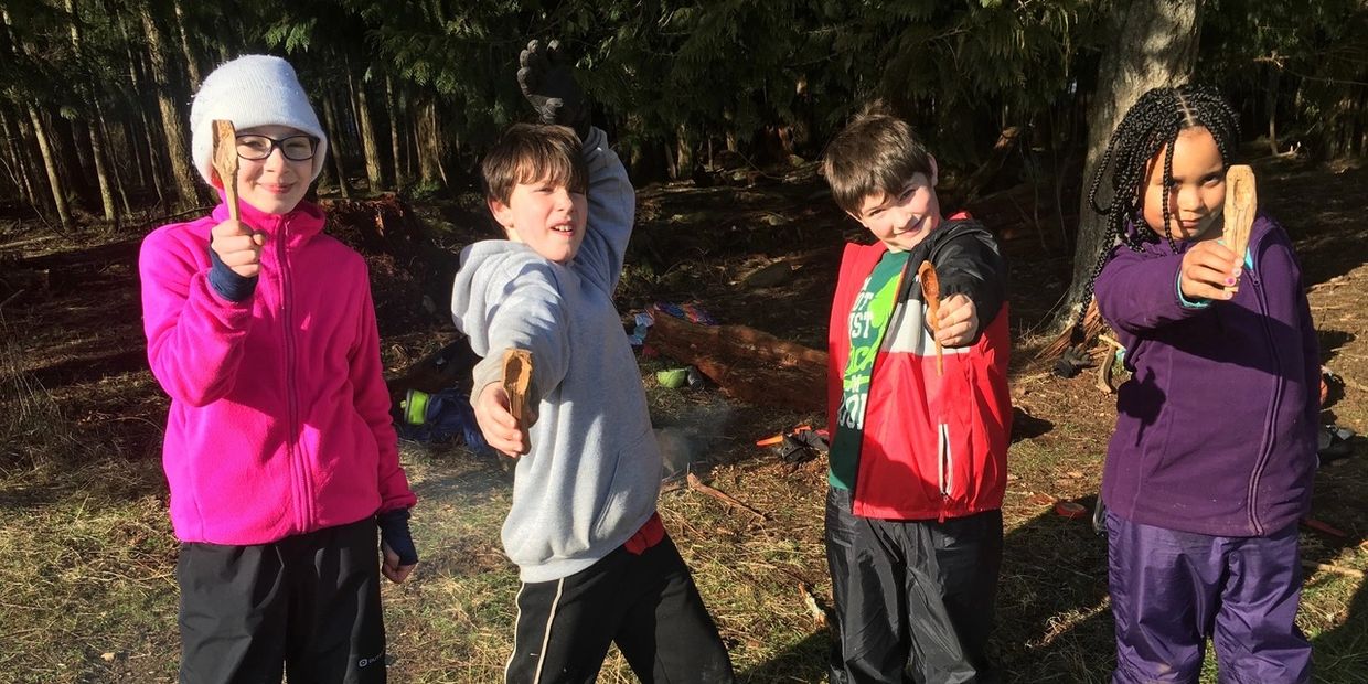 Four kids outdoors holding sticks and smiling.