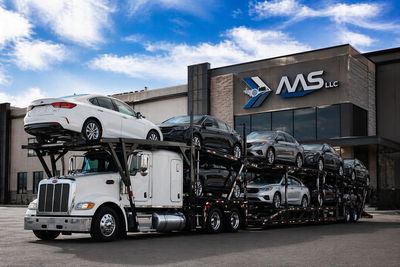 Auto carrier loaded with vehicles parked in front of a modern buildind with a AAS logo on the front 