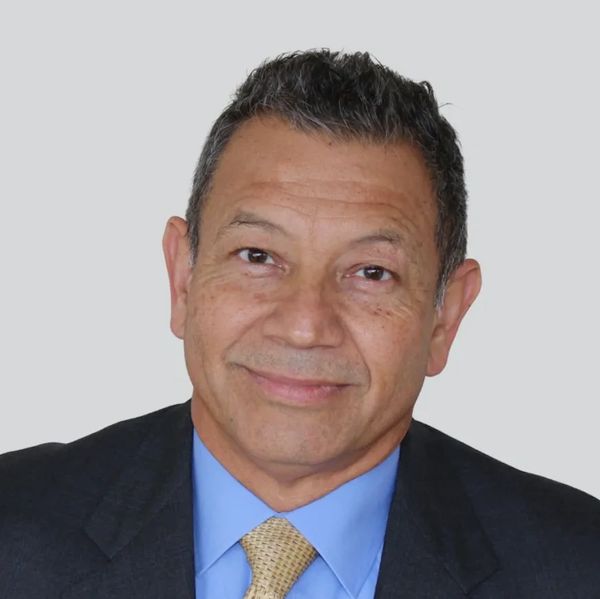 Smiling middle-aged man in a suit and tie against a plain background.