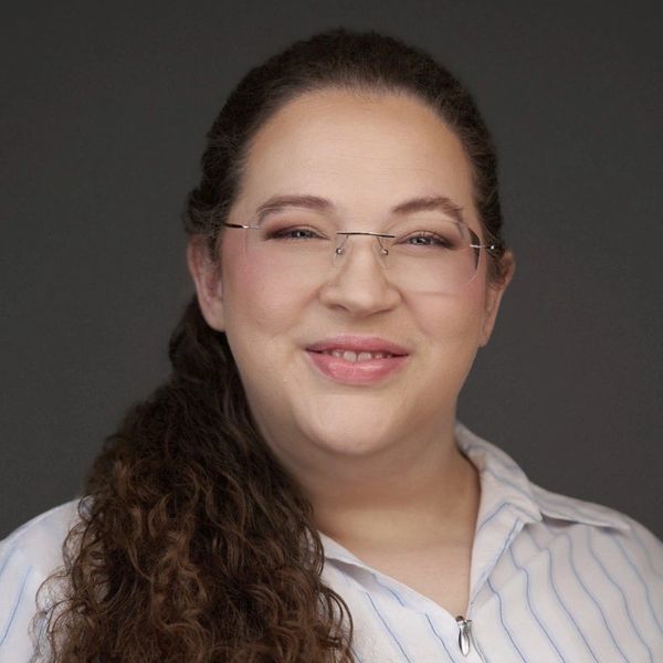 Smiling woman with glasses and curly hair in a striped shirt.