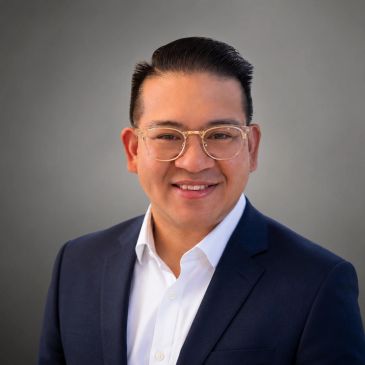 Smiling man in glasses and suit against gray background.