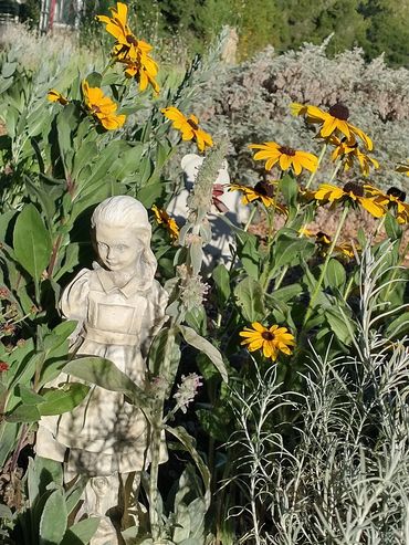 little girl statue surrounded by yellow flowers with green leaves
