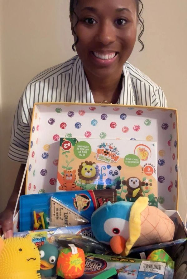Smiling woman holding a box of colorful toys.