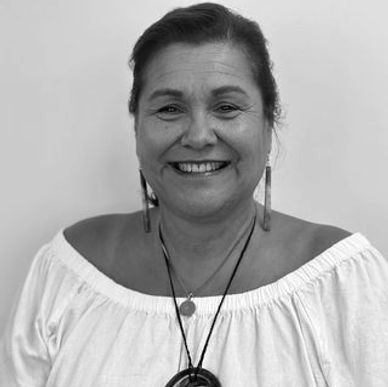 Smiling woman in a white off-shoulder top with earrings and necklaces.