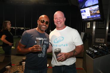 Two men smiling and enjoying drinks at a nighttime event.