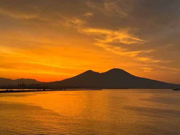 Sunset behind a mountain over calm water with golden sky.
