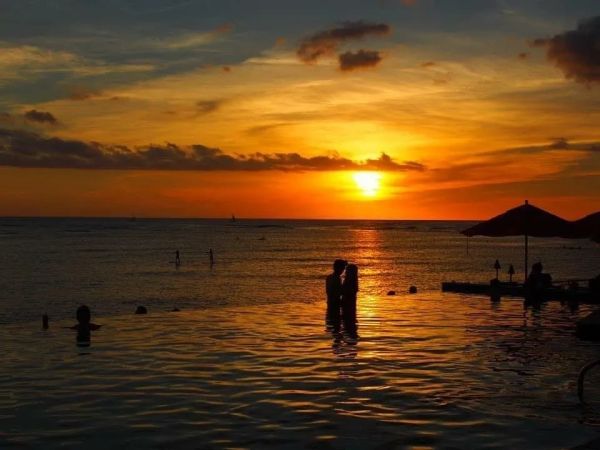 Couple embracing in water during a vibrant sunset at the beach.
