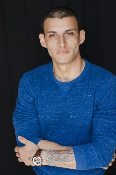 Man in blue sweater with tattoo and watch.