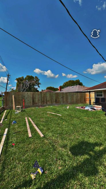 Backyard construction with wood planks and power drill on green grass under a blue sky.
